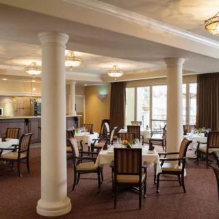 A spacious dining area with elegant decor, featuring tables and chairs arranged symmetrically around classic pillars.