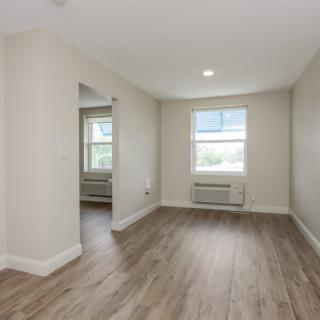 An empty, well-lit living room with wooden flooring and a window.