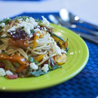 A vibrant plate of pasta topped with assorted vegetables and cheese, served on a green dish.