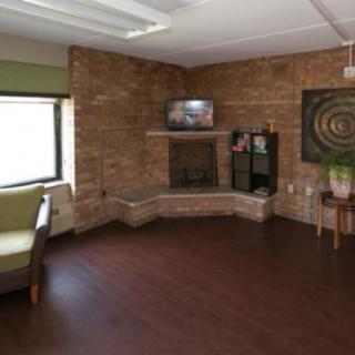 A cozy living room with a brick wall, featuring a fireplace and a television above it. The space has wooden flooring and a seating area.