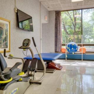 A fitness room with exercise equipment, including a stationary bike and therapy table, next to a large window.