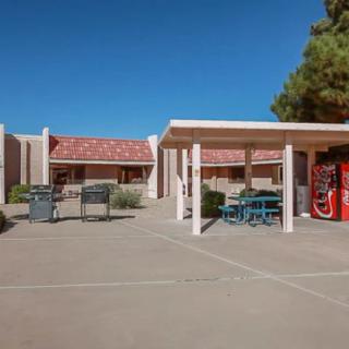 An outdoor patio area featuring tables, chairs, and a vending machine under a clear blue sky.