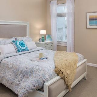 A cozy bedroom with a neatly made bed, a side table lamp, and tasteful decor.