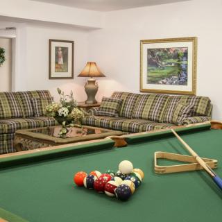 A cozy living room with a billiard table and comfortable sofas, decorated with artwork and a lamp.