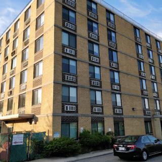 A four-story brick apartment building with multiple windows, situated in an urban environment.