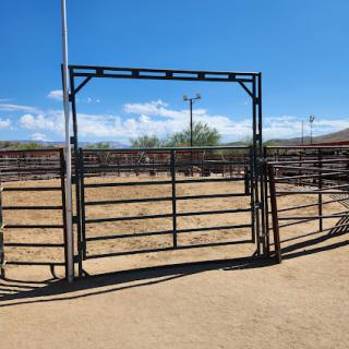 An open gate leading into a corral under a clear blue sky.