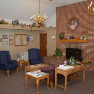 A cozy living room featuring a brick fireplace, wooden furniture, and blue chairs, adorned with decorative items.