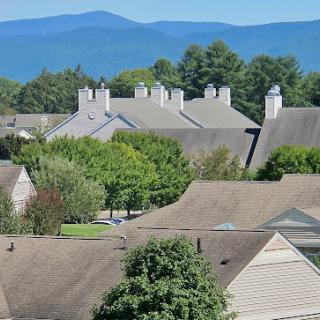 A scenic view of rooftops with mountains in the background and greenery surrounding the area.