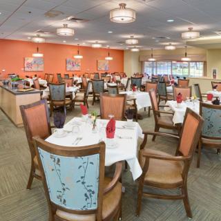 A spacious dining area with multiple tables and chairs, elegantly set for a meal, under softly lit ceiling lights.