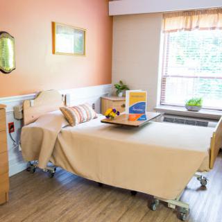 A well-lit and inviting hospital patient room featuring a bed, bedside table, and a window.