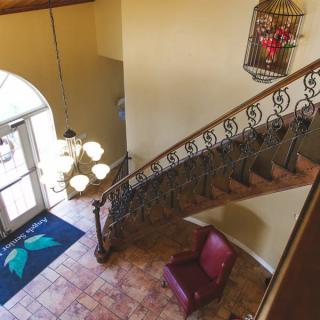 A view of a stylish foyer featuring a wrought iron staircase, elegant chandelier, and comfortable armchair.