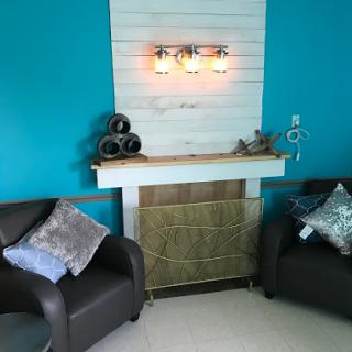 A cozy living room featuring stylish black chairs, a decorative shelf with warm lighting, and vibrant blue walls.