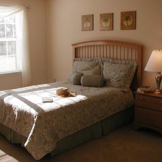 A cozy, well-lit bedroom with a neatly made bed and a bedside lamp.