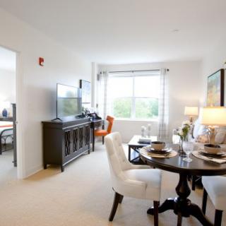 A bright and modern living room with a dining area, featuring elegant furniture and a large window.
