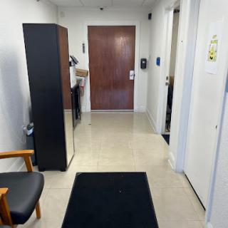 A view of a hallway in an office setting, showcasing a refrigerator and wooden door.