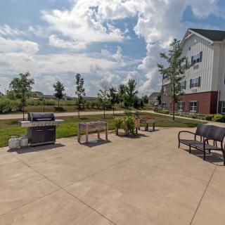 A sunny outdoor patio area featuring benches, grills, and a building in the background.