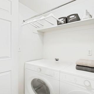 A clean and organized laundry room featuring a washing machine, dryer, and shelving for storage.