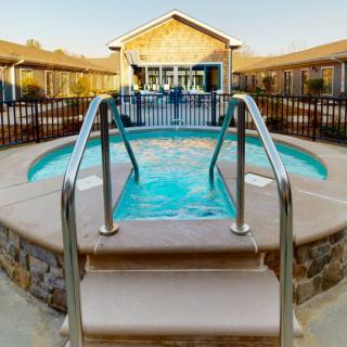 A small circular outdoor pool with metal steps and railing, surrounded by a fence, situated near a building during the day.