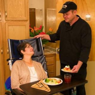 A caregiver assists an elderly person with meal service in a healthcare setting.