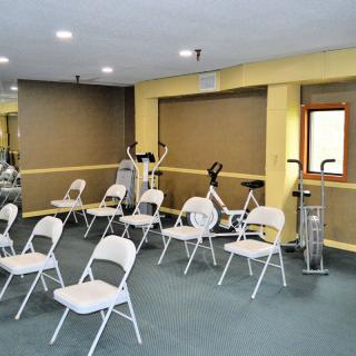A room with folding chairs arranged for a meeting, featuring exercise equipment in the background.