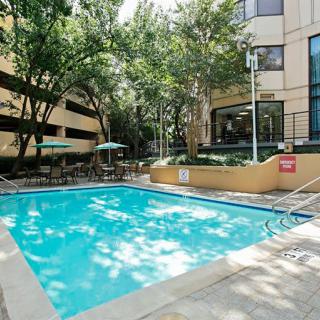 A serene outdoor swimming pool surrounded by trees and seating areas with umbrellas.