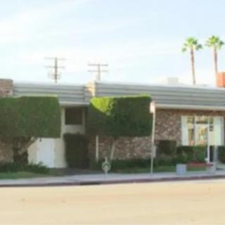 A mid-century modern building with brick walls and trimmed hedges under a clear sky.