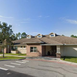 A suburban residential building with a driveway and trees, under a clear blue sky.