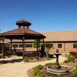 A scenic garden with a gazebo and fountain next to a brick building.