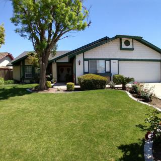 A suburban house with a well-maintained lawn and a large tree in the front yard.