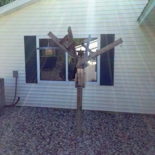 A wooden sculpture stands in front of a house, illuminated by sunlight.