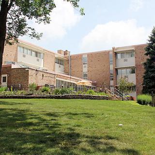A brick apartment building with a well-maintained lawn and surrounding trees.