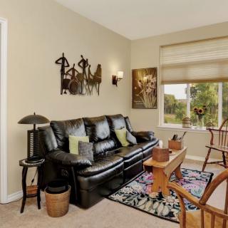 A cozy living room with a black leather sofa, wooden chairs, and decorative wall art.
