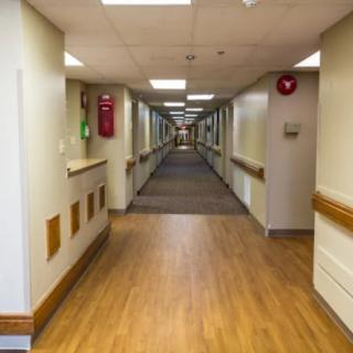 A view down a long, well-lit hospital corridor with wooden flooring.