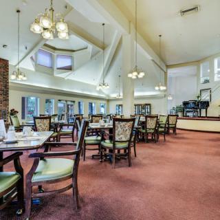 A spacious dining room with elegantly arranged tables and chairs, featuring large windows and chandeliers.