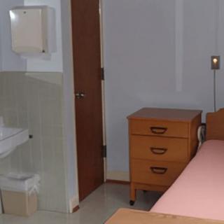 A simple hospital room with a bed, nightstand, and sink.