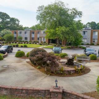 A residential building with a landscaped parking lot featuring several parked cars and surrounding trees.