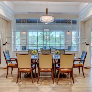 A spacious dining room with a large table and elegant chairs, featuring a chandelier and large windows.