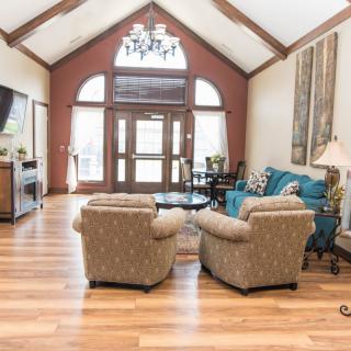 A spacious living room with elegant furniture and high ceilings, featuring cozy armchairs and a sofa on polished wood flooring.