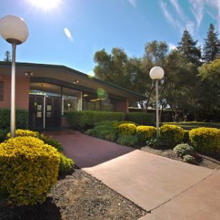 A welcoming entrance to a landscaped building, illuminated by natural sunlight.