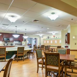 A well-lit dining area with tables and chairs, adjacent to a kitchen.