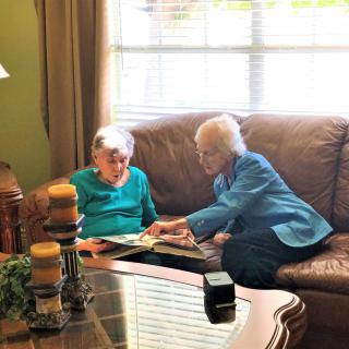 Two elderly individuals sitting on a couch, looking at a photo album in a cozy living room.
