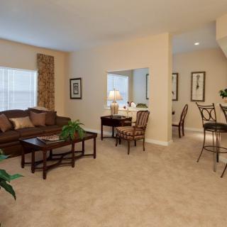 A cozy living room with a sofa, tables, and chairs arranged on a carpet.