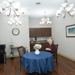 A cozy indoor space featuring a blue table with flowers and a person seated in a well-lit room.