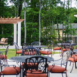 A serene outdoor patio area with tables, chairs, and a pergola surrounded by lush greenery.