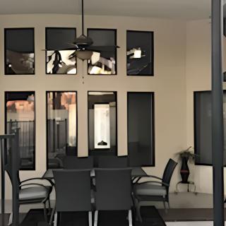 A modern patio area featuring a dining table set with chairs, large windows, and a ceiling fan.