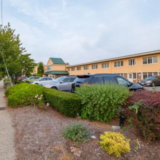 A hotel with a parking lot and landscaped hedges in front.