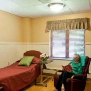 An elderly person sits in a chair in a comfortably furnished room.