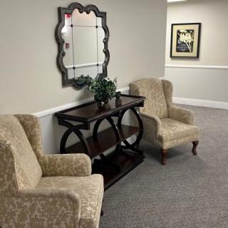 A cozy hallway setup featuring two upholstered chairs, a decorative table with a plant, and a wall-mounted mirror.