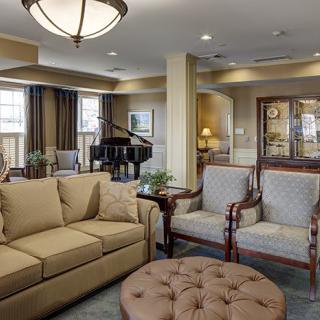 A cozy and elegant living room featuring a comfortable sofa, armchairs, a grand piano, and tasteful decor.