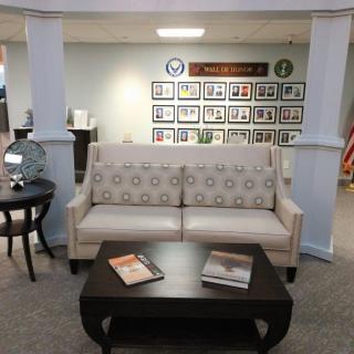 A comfortable lounge area featuring a patterned couch, coffee table with magazines, and framed photos on the wall.